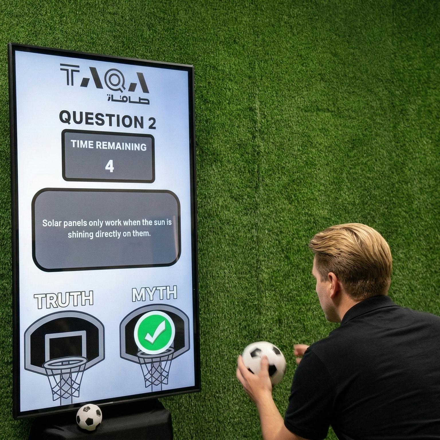 A guest throwing a softball at a large digital Truth or Myth display screen to lock in an answer at a high-energy corporate exhibition booth activation